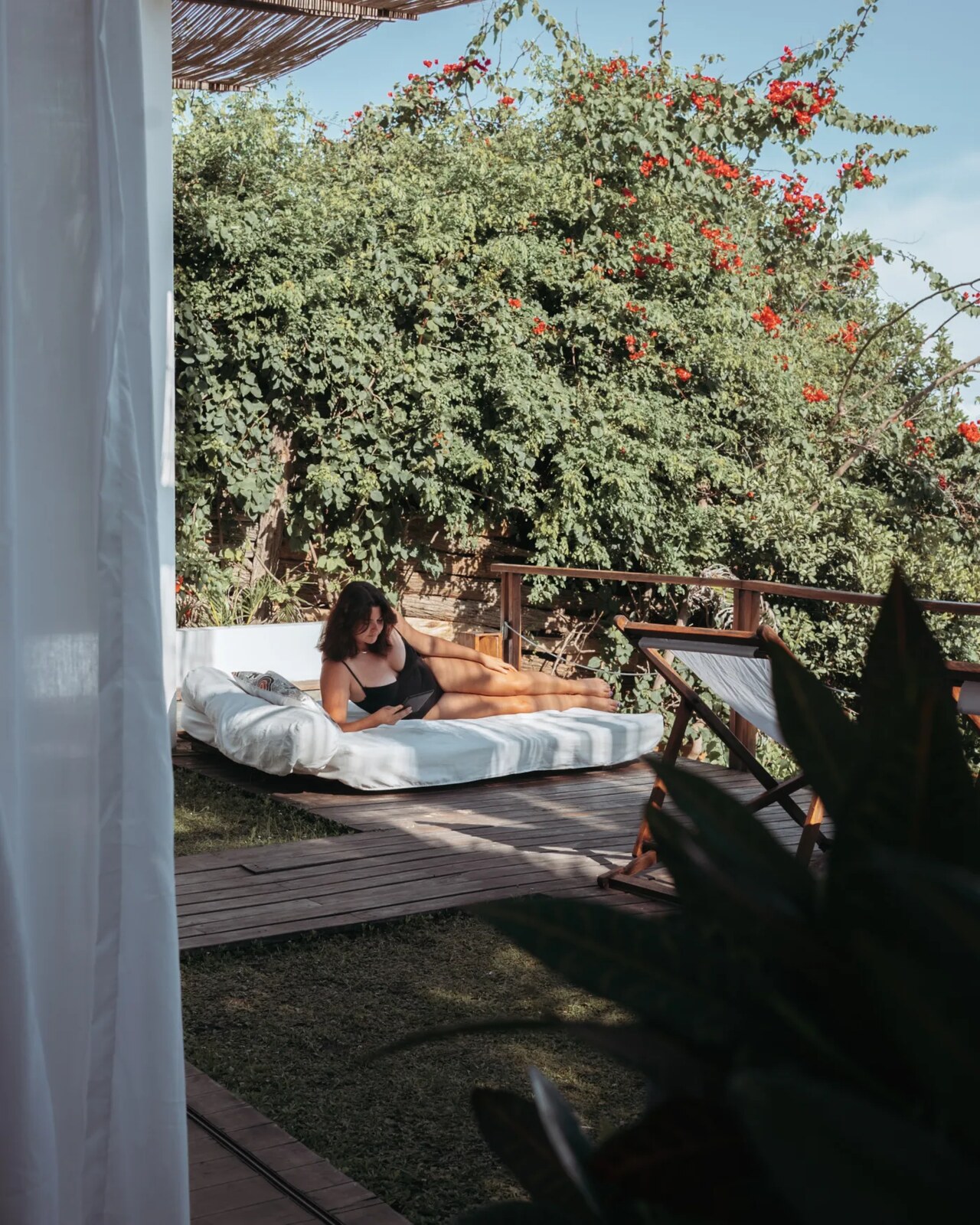 Guest relaxing on a daybed on a deck framed by bougainvillea with sea views at Duna Sonâmbula, Tofo, Mozambique