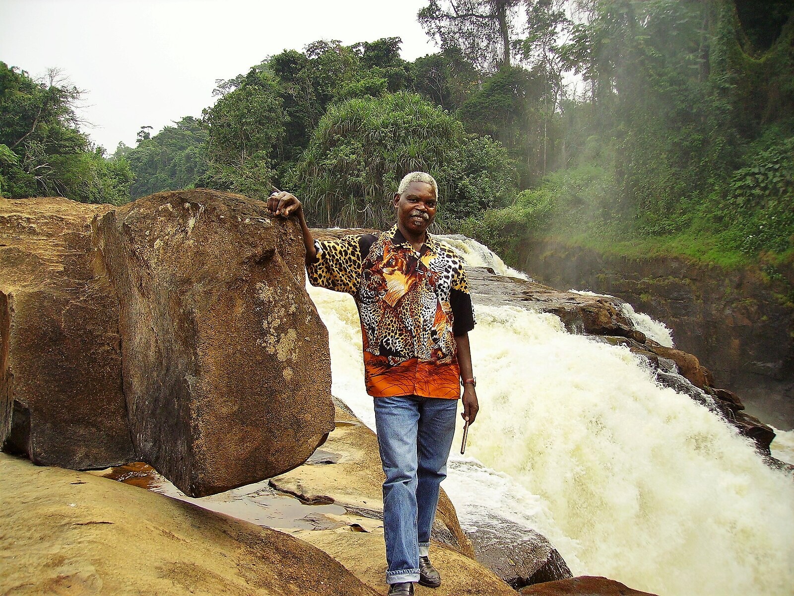 Loufoulakari Falls in full flow — the Loufoulakari River pours over a wide basalt shelf into a forested ravine 80 km from Brazzaville, with a visitor on the rocks giving a sense of scale