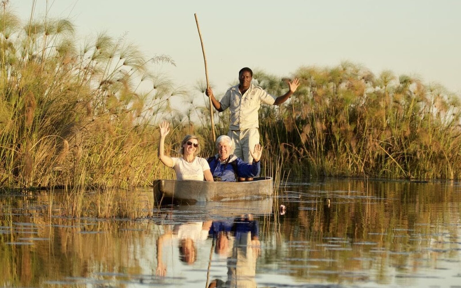 A couple gliding through the reed-lined channels of the Okavango Delta in a mokoro at golden hour