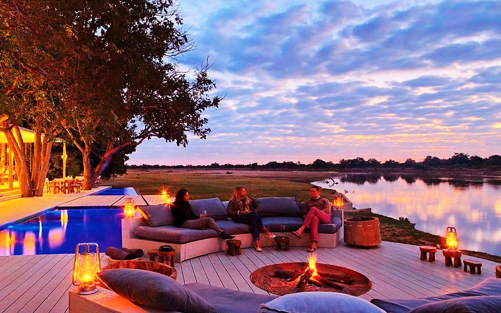 A suite and deck glowing at dusk overlooking the river at Chinzombo in Zambia's South Luangwa