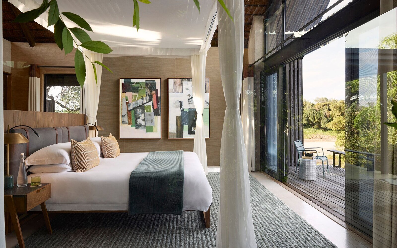 A luxury bush suite bedroom opening through glass doors onto a private deck over the river in the greater Kruger