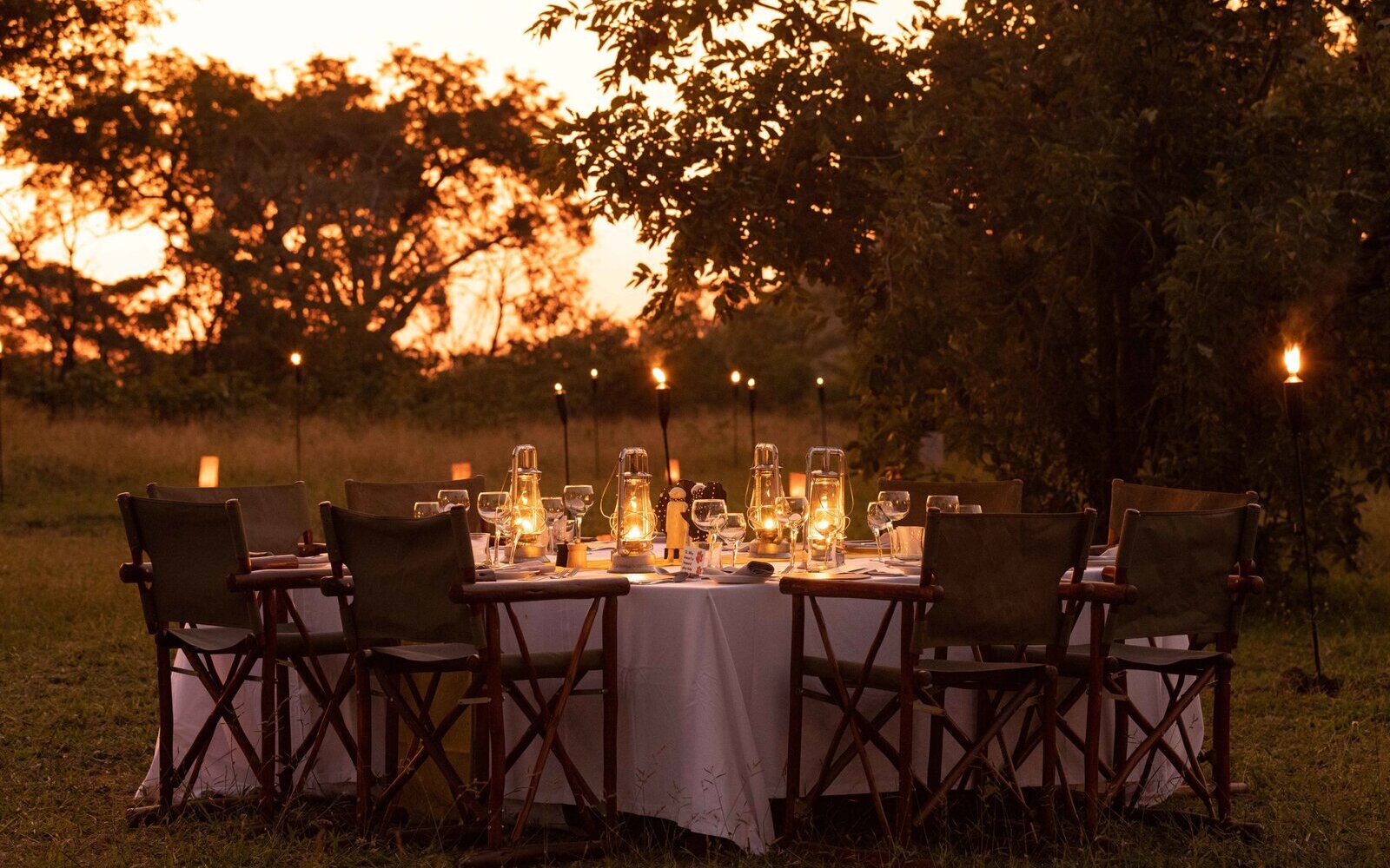 A candlelit private bush dinner set with lanterns in a clearing at golden dusk in the greater Kruger