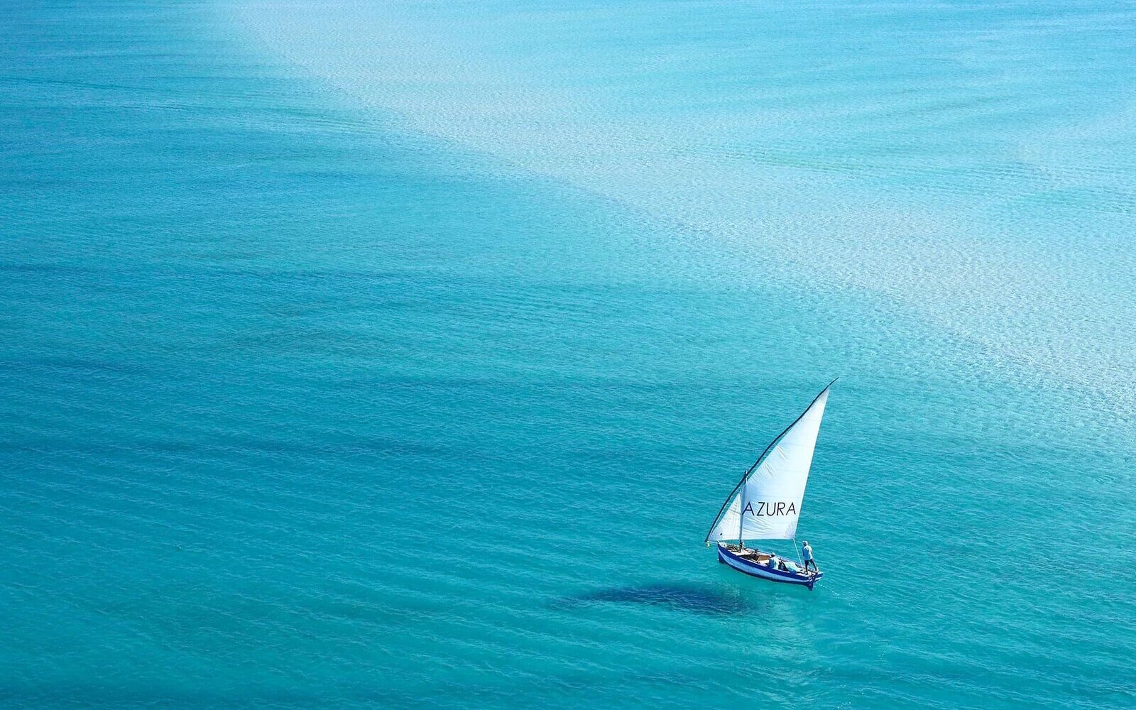 A traditional white-sailed dhow on brilliant turquoise water off the Mozambique islands