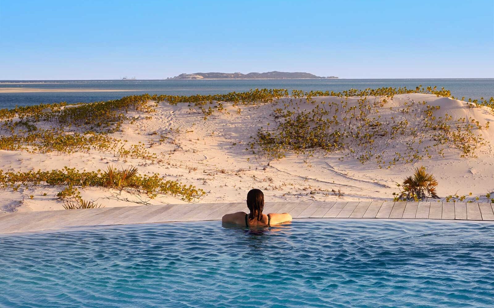 A person floating in an infinity pool that seems to merge with the lagoon and dunes at Kisawa Sanctuary