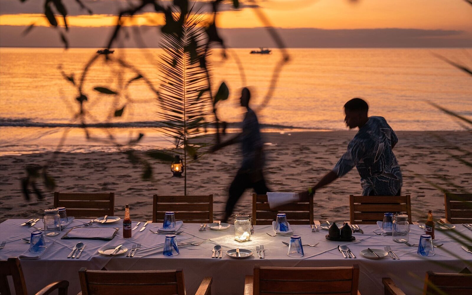 A beach table being set with lanterns for a private dinner at golden sunset on a Mozambique beach