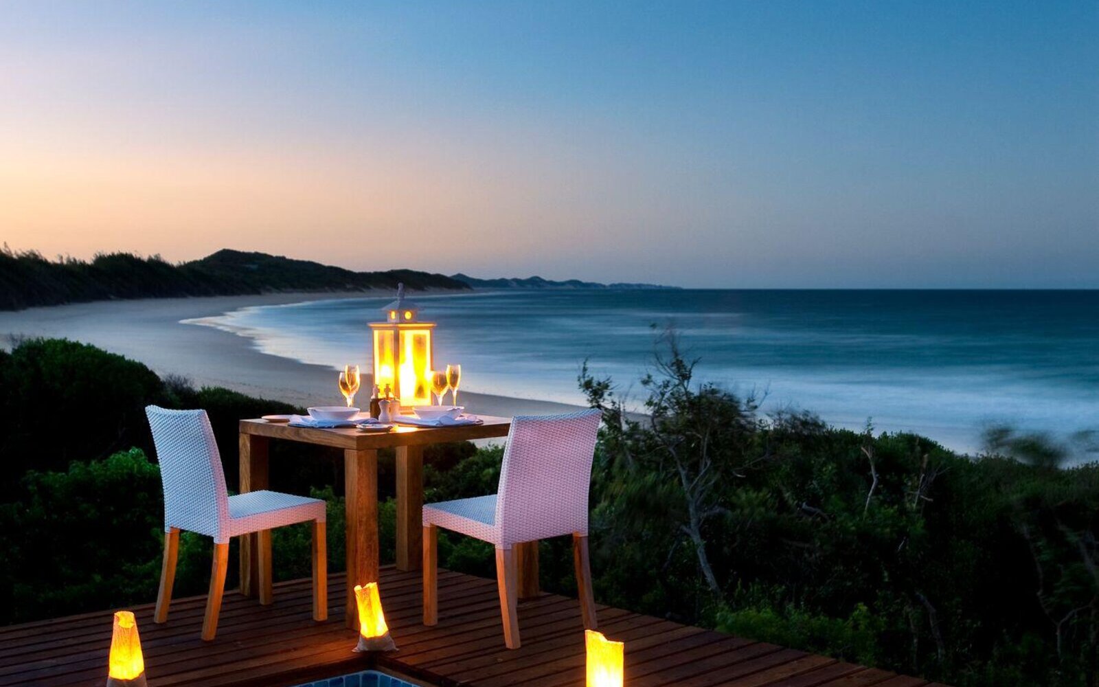 A candlelit dinner table for two set on a deck above the ocean at dusk at White Pearl, Mozambique