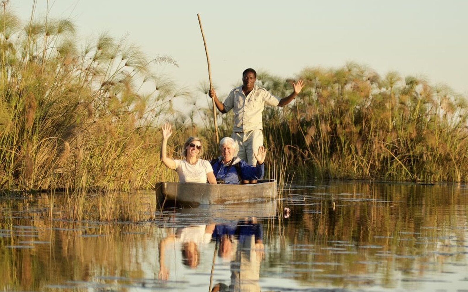 A couple gliding through papyrus-lined channels in a mokoro poled by a guide in golden delta light