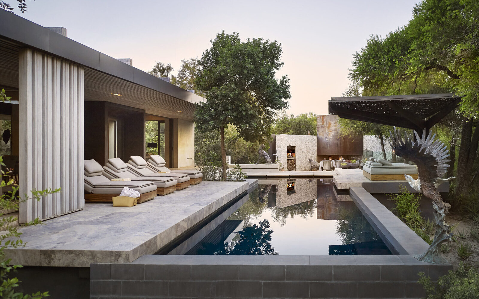 The sleek architectural pool and loungers of a Plains House at Cheetah Plains, framed by glass, stone and bush