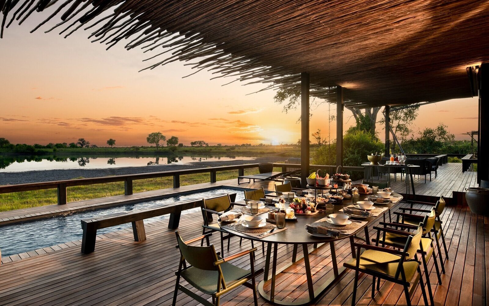 An open-sided dining deck at Dulini laid for a meal, overlooking the Sand River at sunset