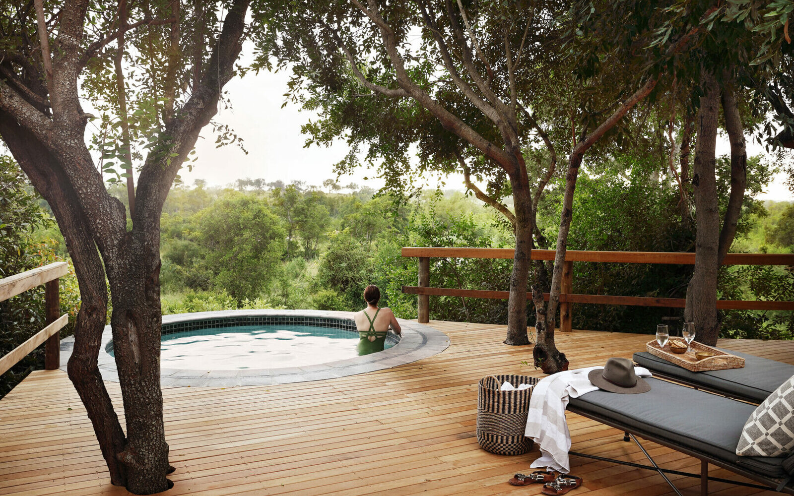 A couple relax in a private plunge pool on a timber deck shaded by riverine trees at Londolozi in the Sabi Sand