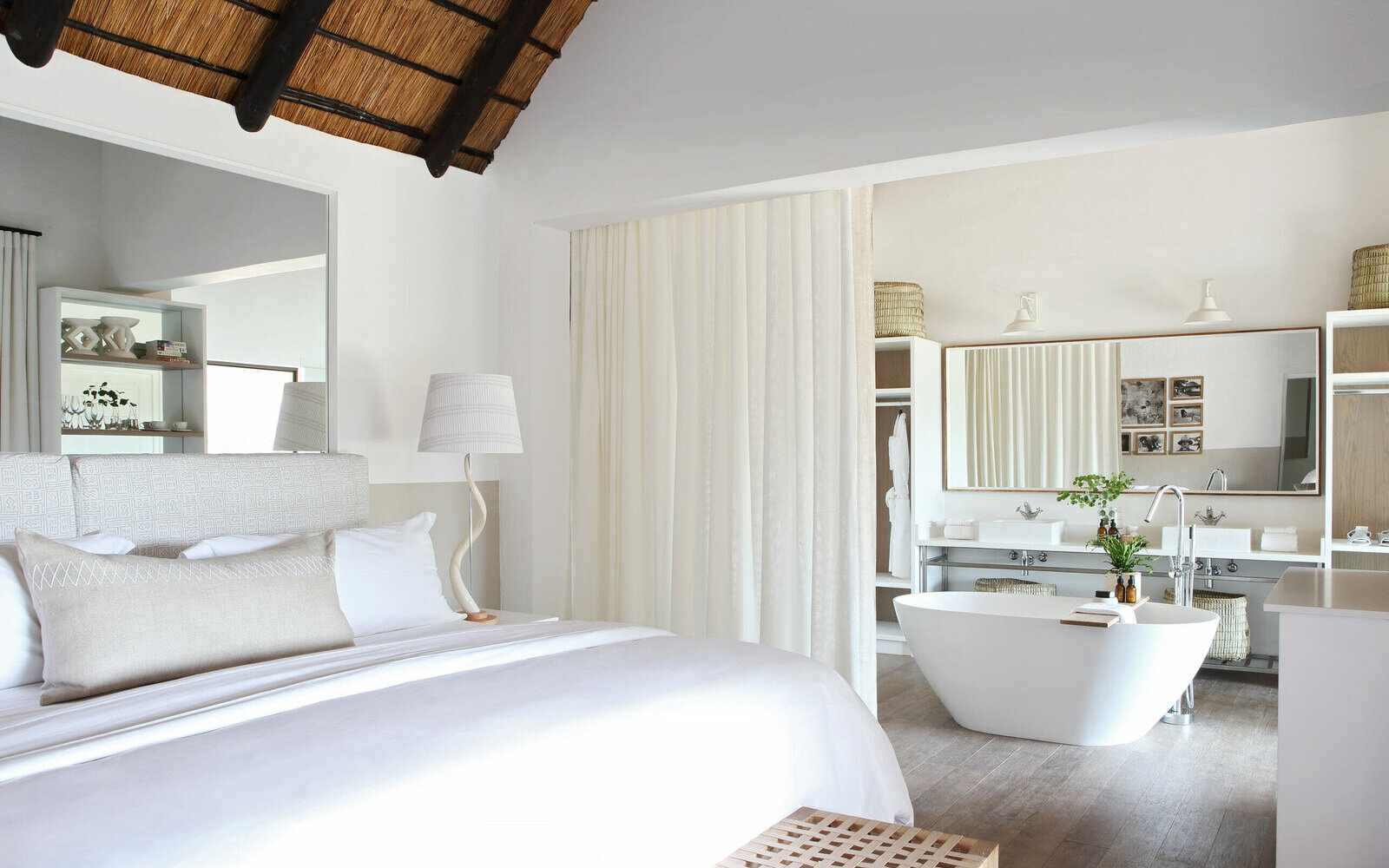 A light-filled suite at Londolozi with a large bed, flowing white drapes and a freestanding bath framed by the bush