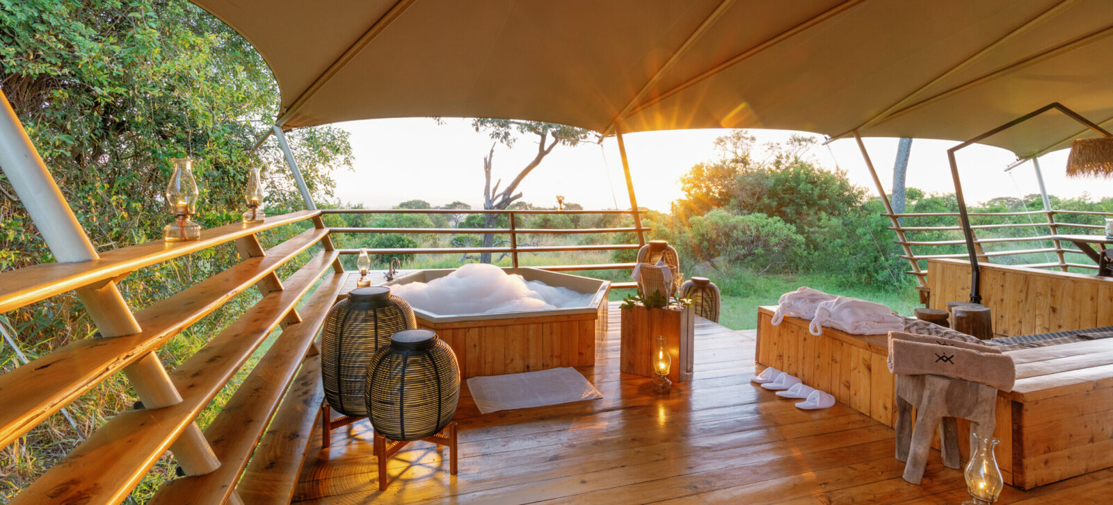 A private tented suite deck at Serengeti Bushtops with an outdoor hot tub and loungers, opening onto the golden Serengeti plains at sunset