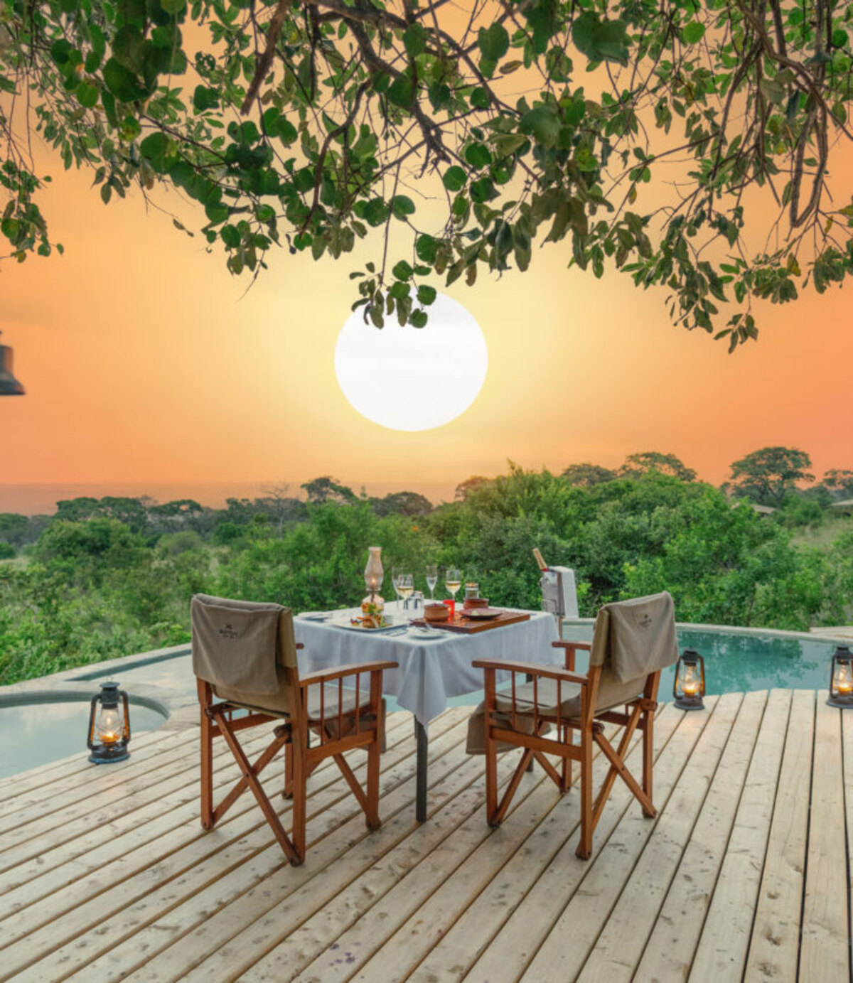 A candlelit table for two set on a private deck above the pool at Serengeti Bushtops, the sun setting orange over the plains beyond