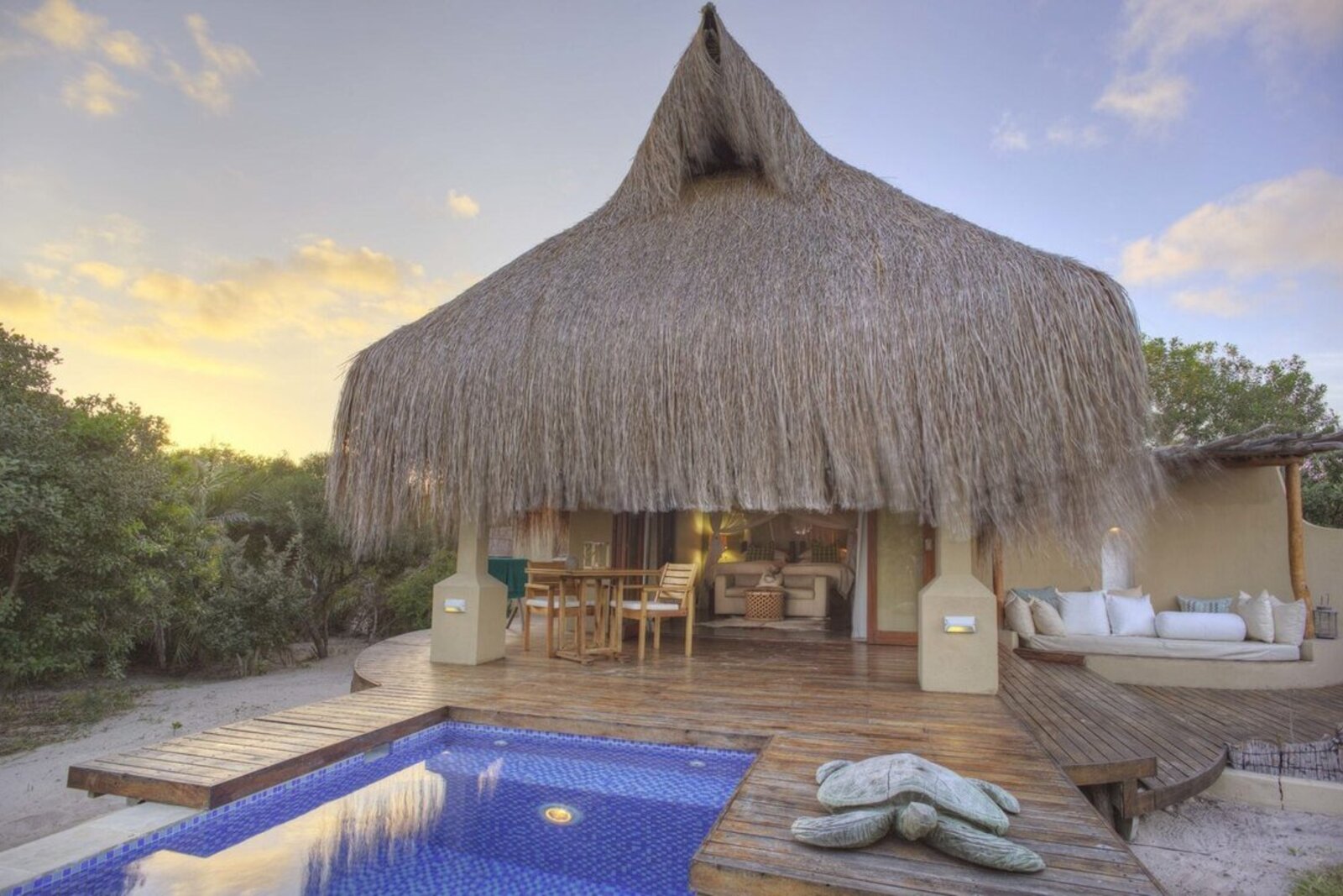 A thatched beach villa with a private plunge pool at sunset on Benguerra Island