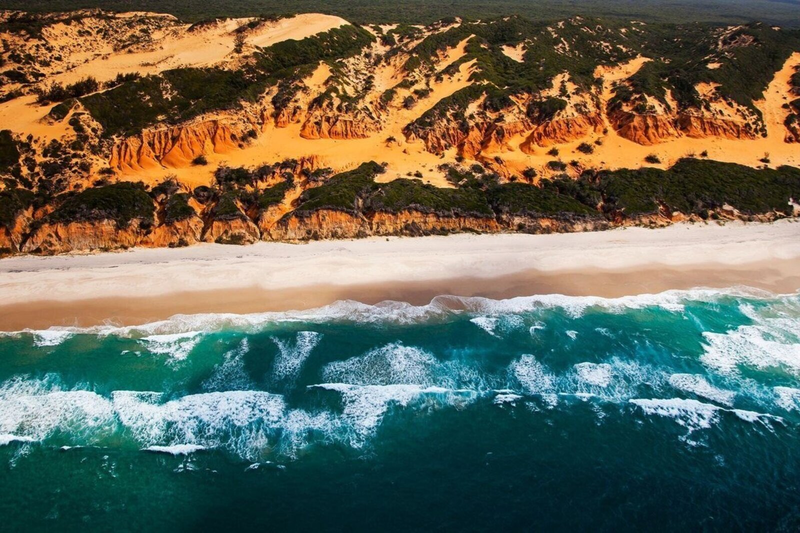 An aerial view of wild dunes meeting turquoise surf on a remote Indian Ocean coast