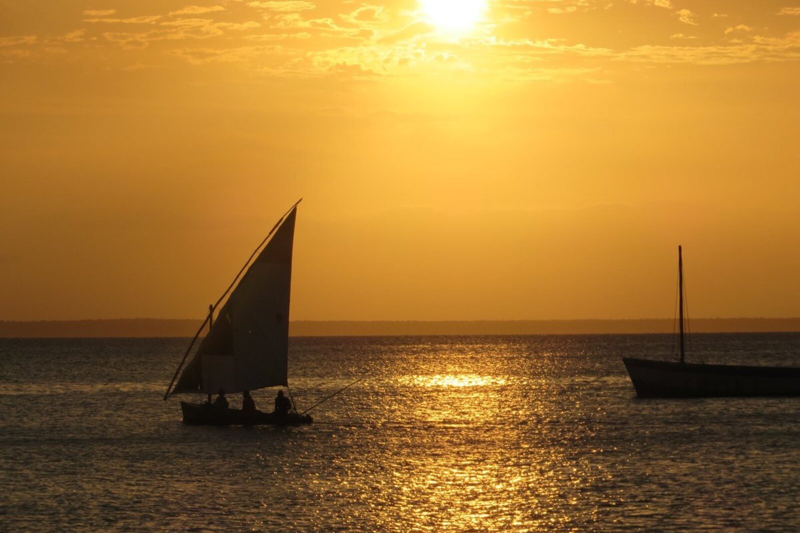 A traditional dhow sailing across a golden Indian Ocean sunset