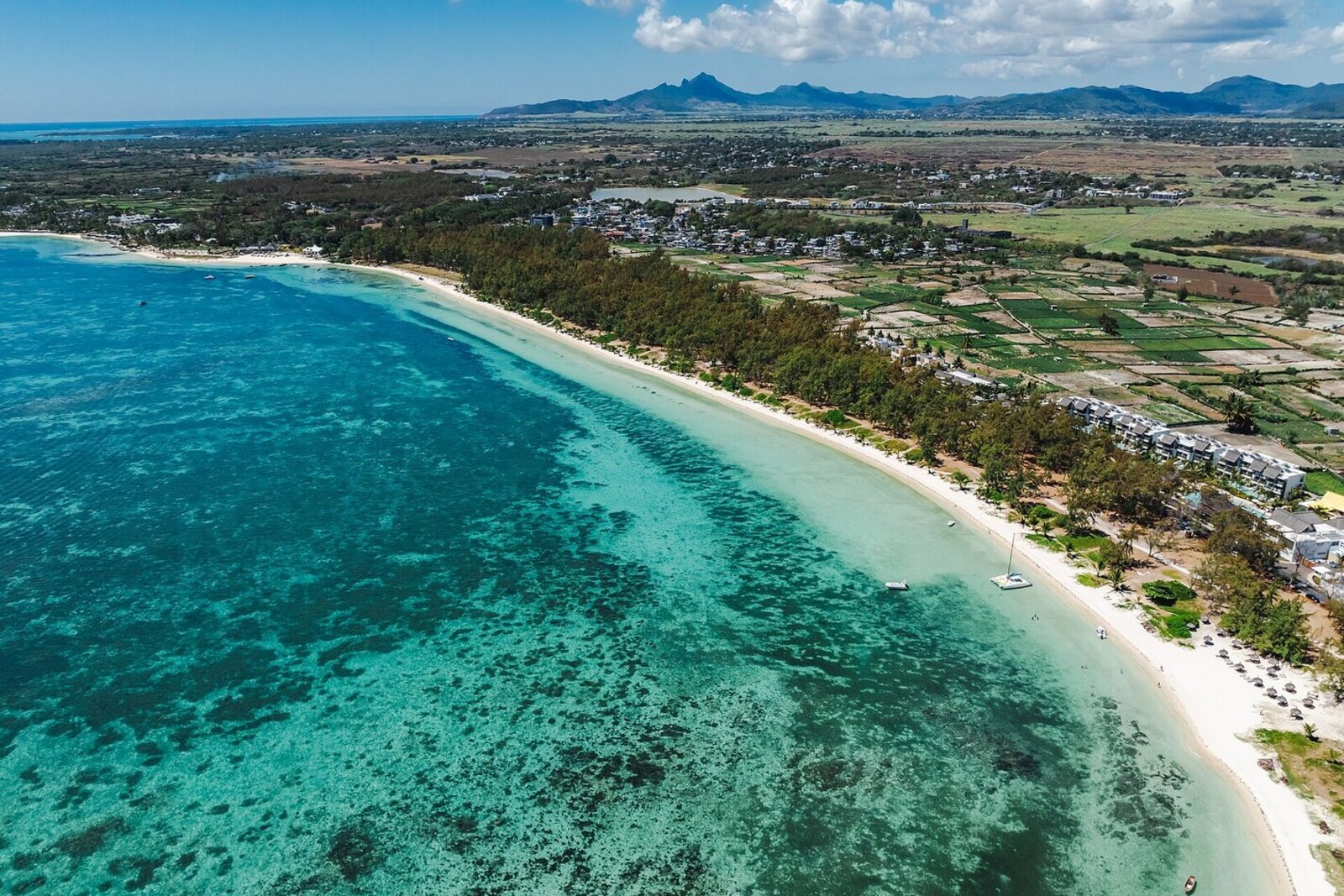 An aerial view of a turquoise Mauritius lagoon fringed by resort and palm-lined beach