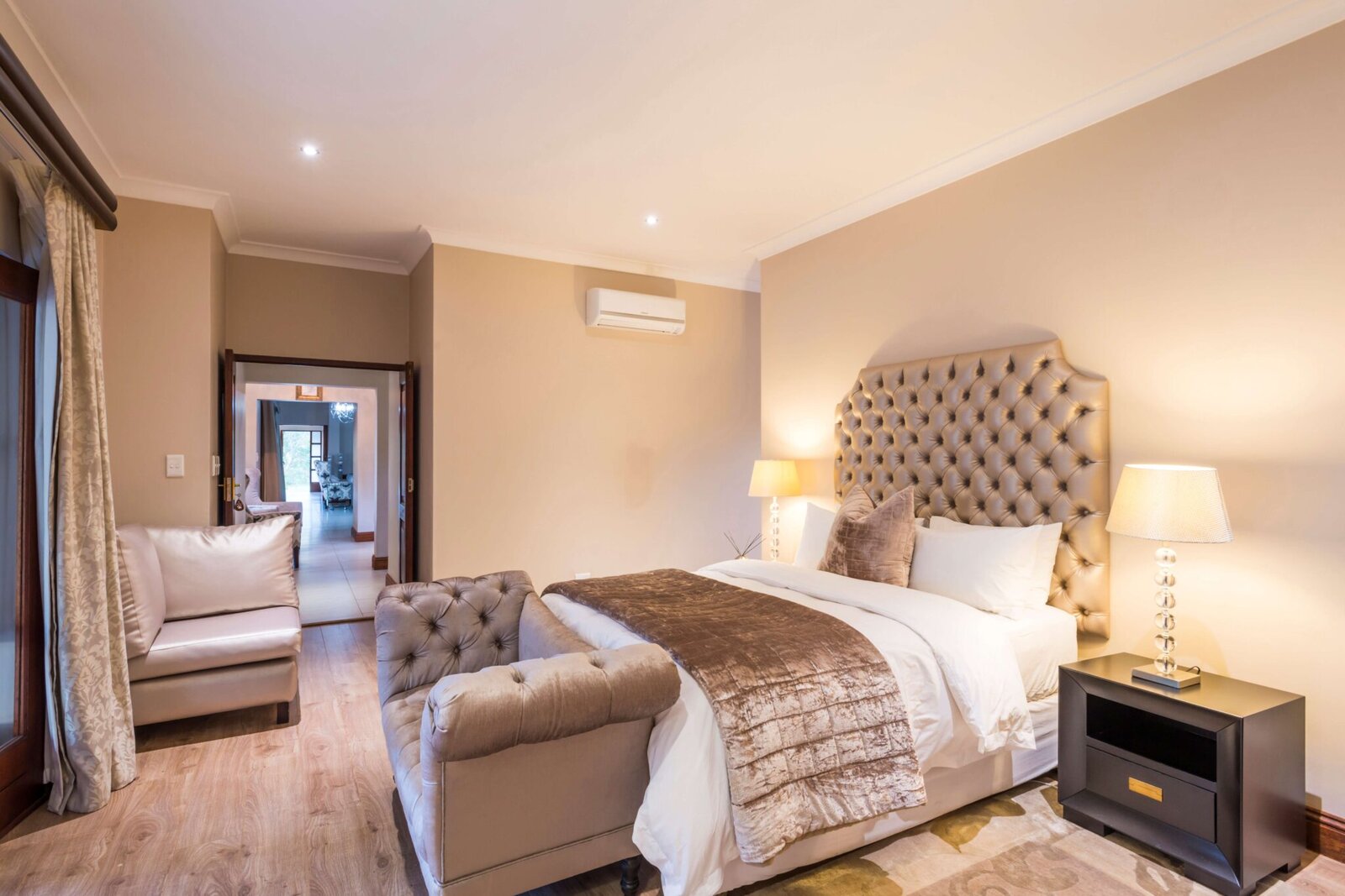 A tufted bed and lamp-lit suite interior opening to the en-suite bathroom at AM Lodge, Greater Kruger