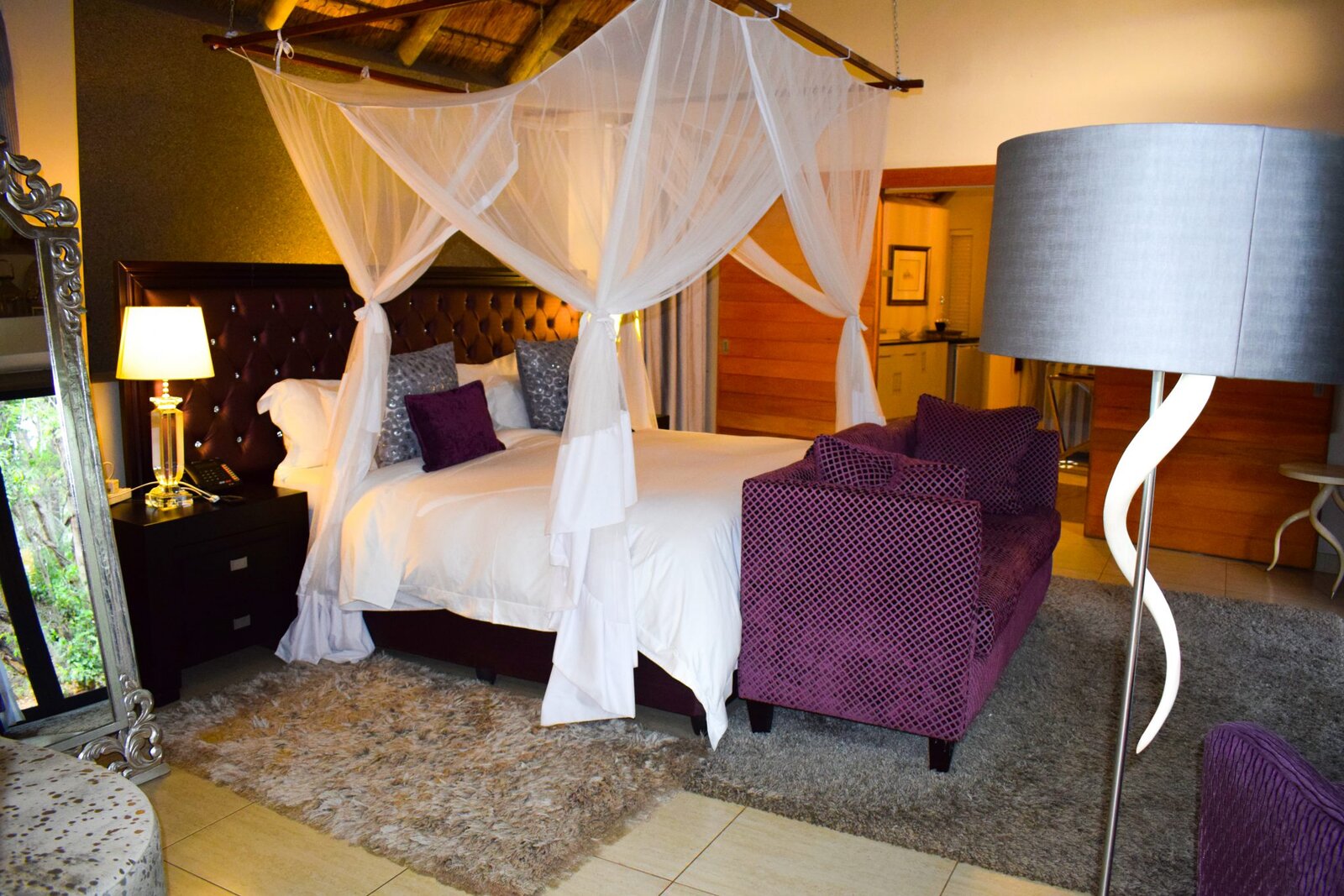 A canopy bed with mosquito-net drapes and purple accents in a suite at AM Lodge near Hoedspruit