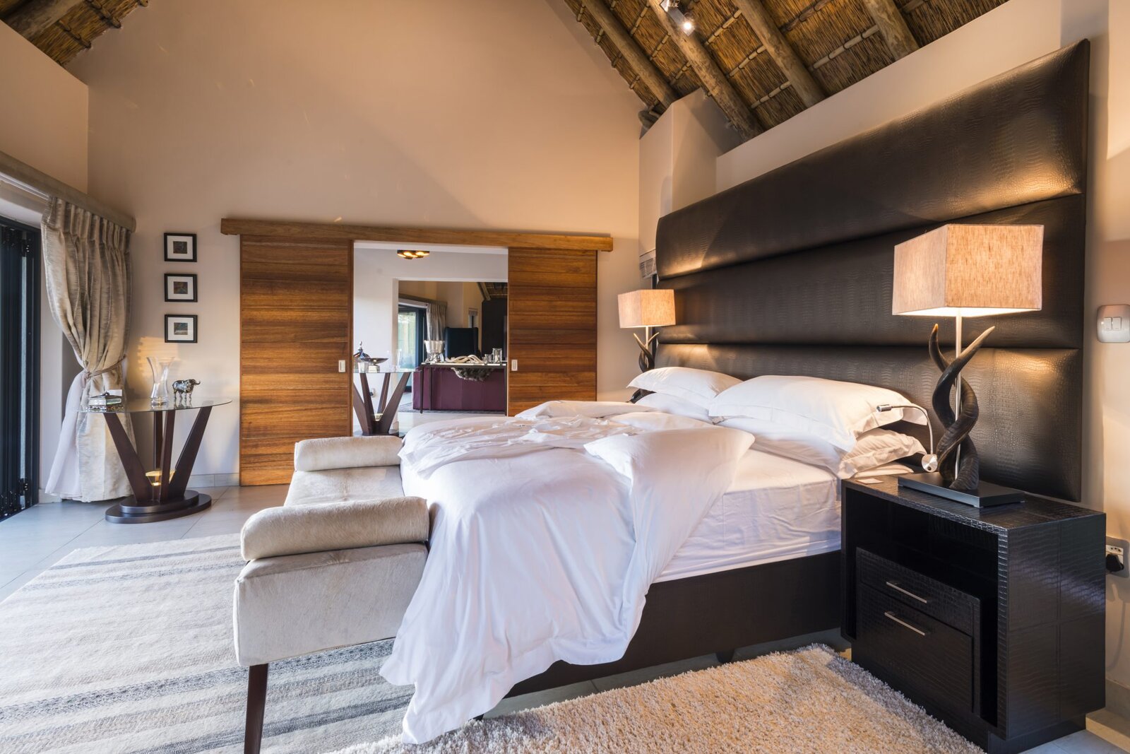 A thatched-roof suite bedroom opening onto a private deck at AM Lodge, Hoedspruit