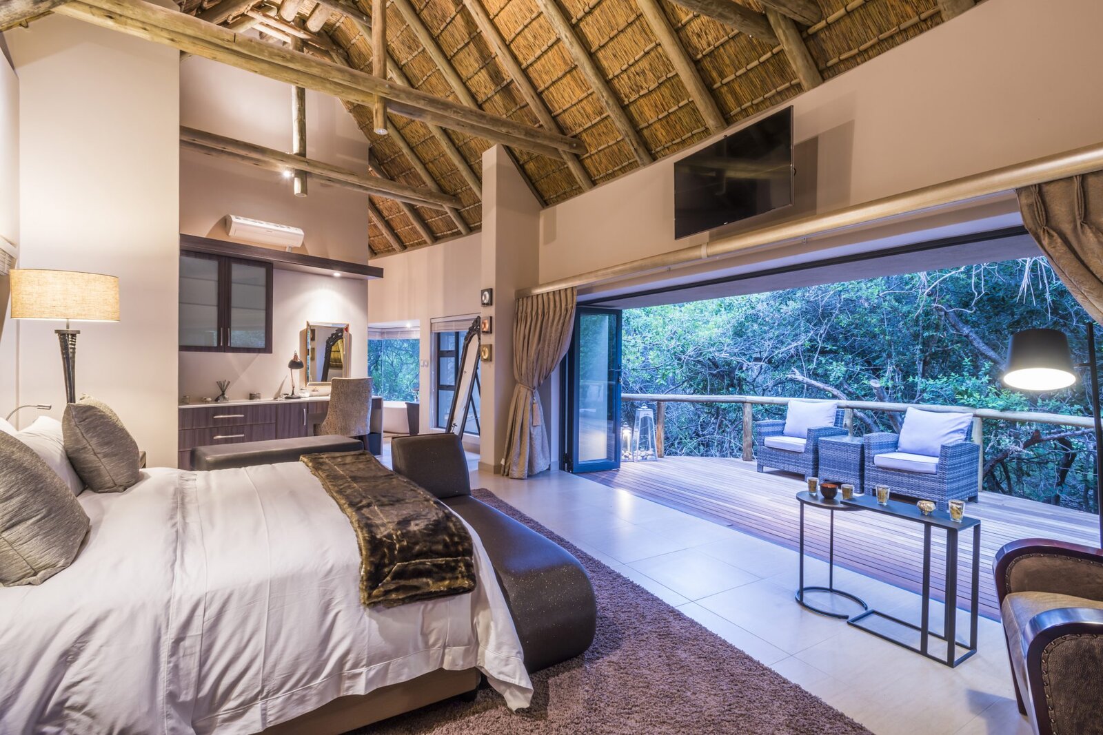 A suite with a television and glass doors to a deck with loungers under thatch at AM Lodge, Limpopo