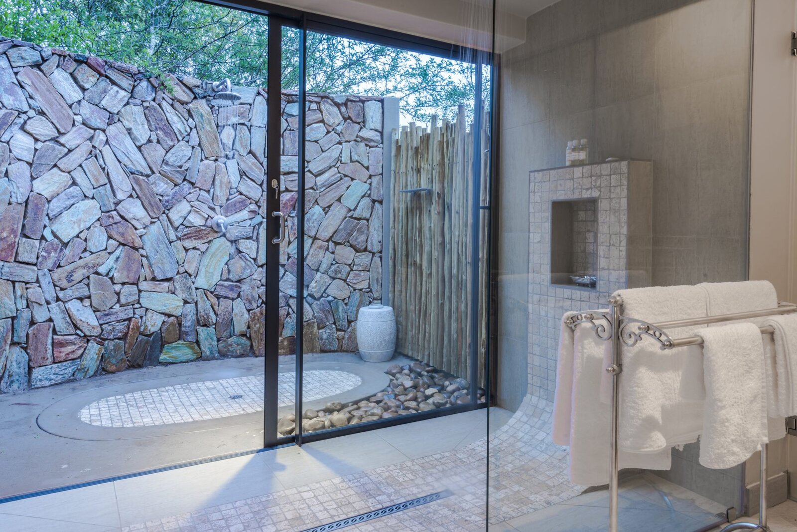 An en-suite bathroom with a glass wall through to an outdoor stone shower on river pebbles at AM Lodge, Hoedspruit