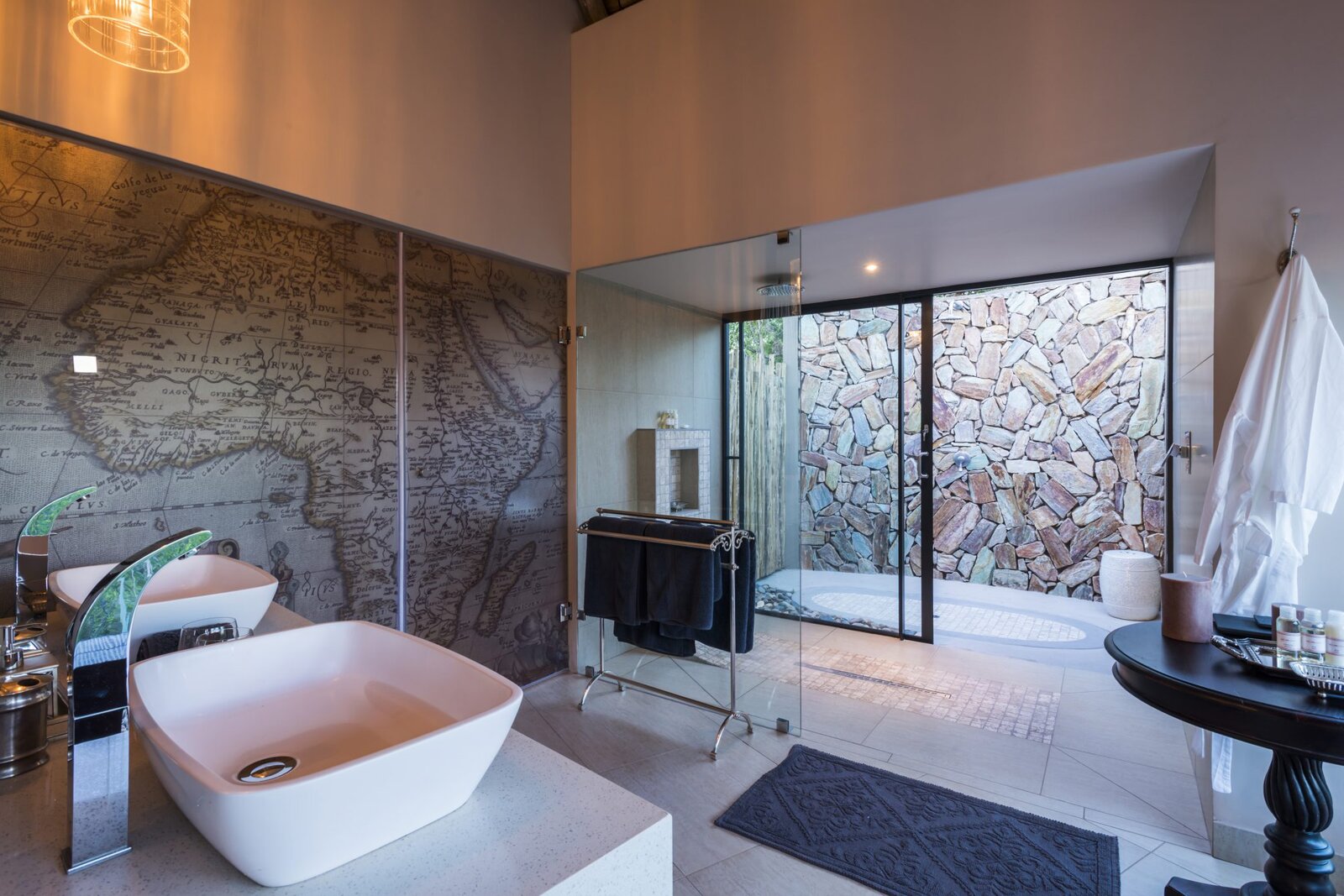 A bath with a map-mural wall and a glass door to an outdoor shower at AM Lodge, Hoedspruit