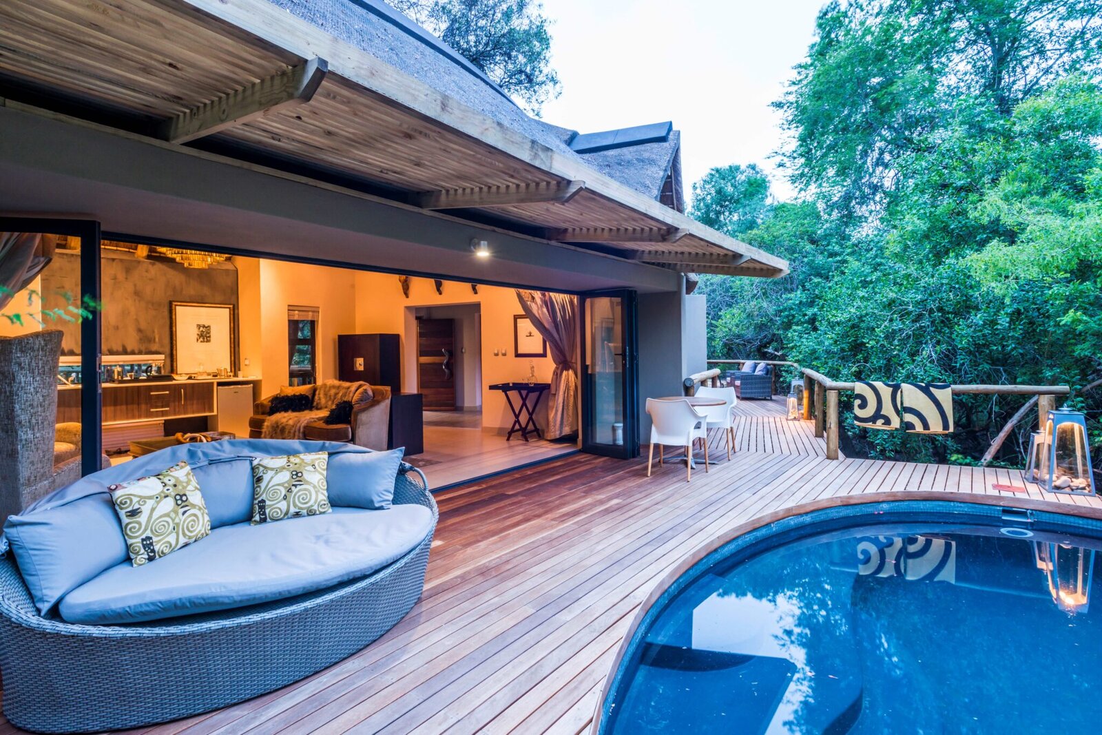 The deck, round daybed and rim-flow pool of AM Lodge lit at dusk with the bush beyond at Hoedspruit