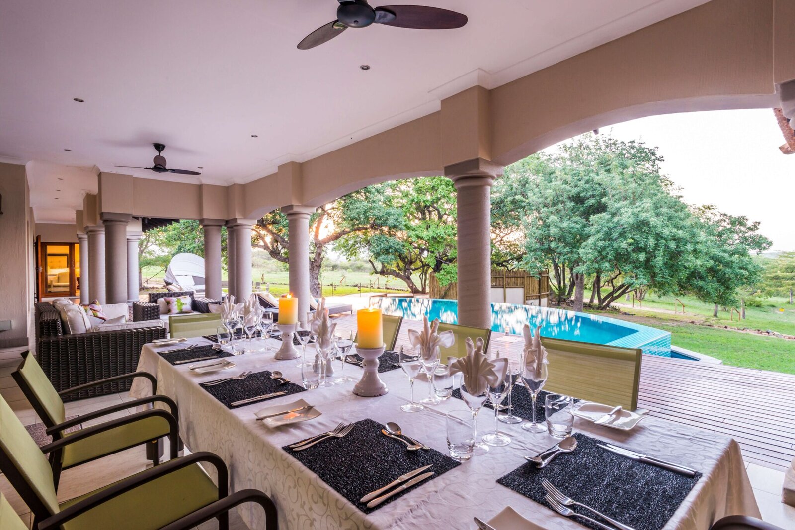 A dining table set under a thatched terrace with the pool beyond at AM Lodge, Klaserie