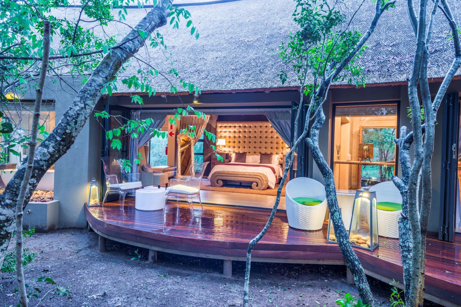 A deck dining set-up at dusk beside the pool with a lit suite behind at AM Lodge, Hoedspruit