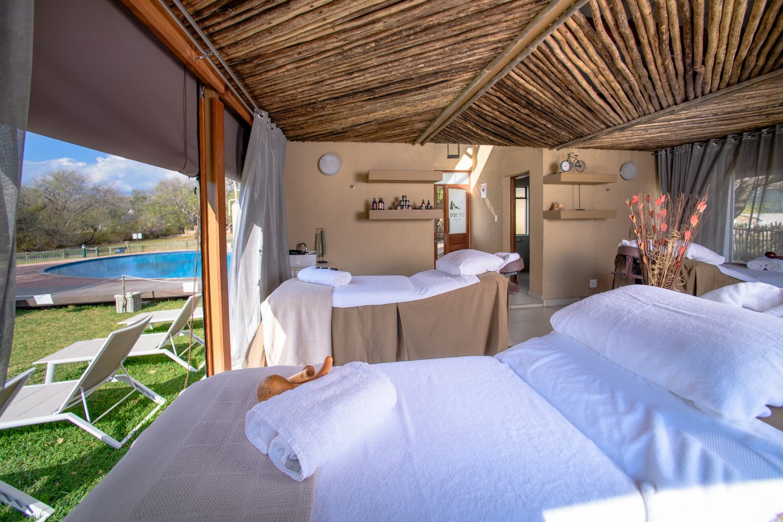 Spa treatment beds set up under thatch beside the pool at the AM Spa, AM Lodge