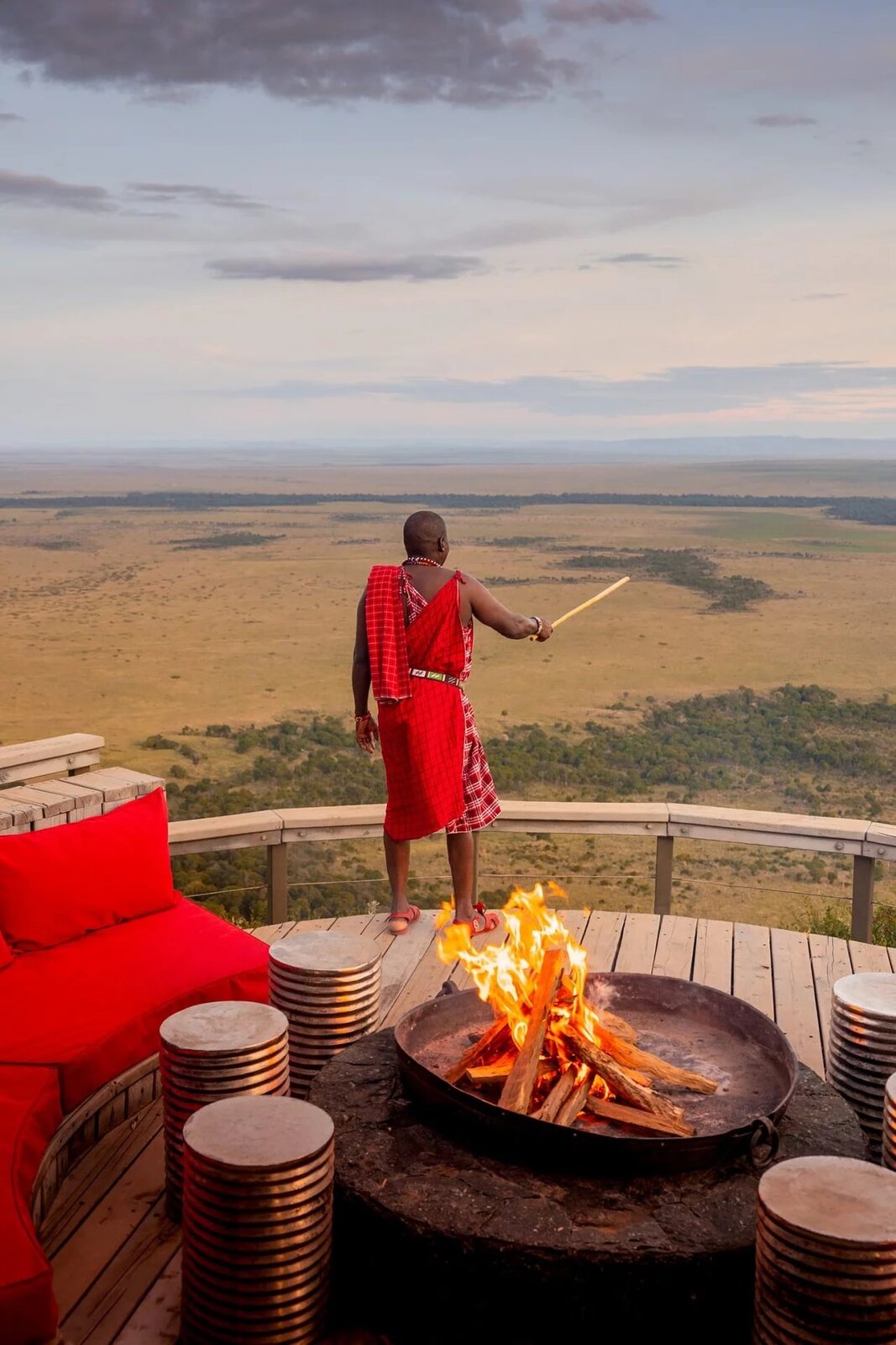 A Maasai warrior at a fire pit at sundown on the edge of the escarpment at Angama Mara