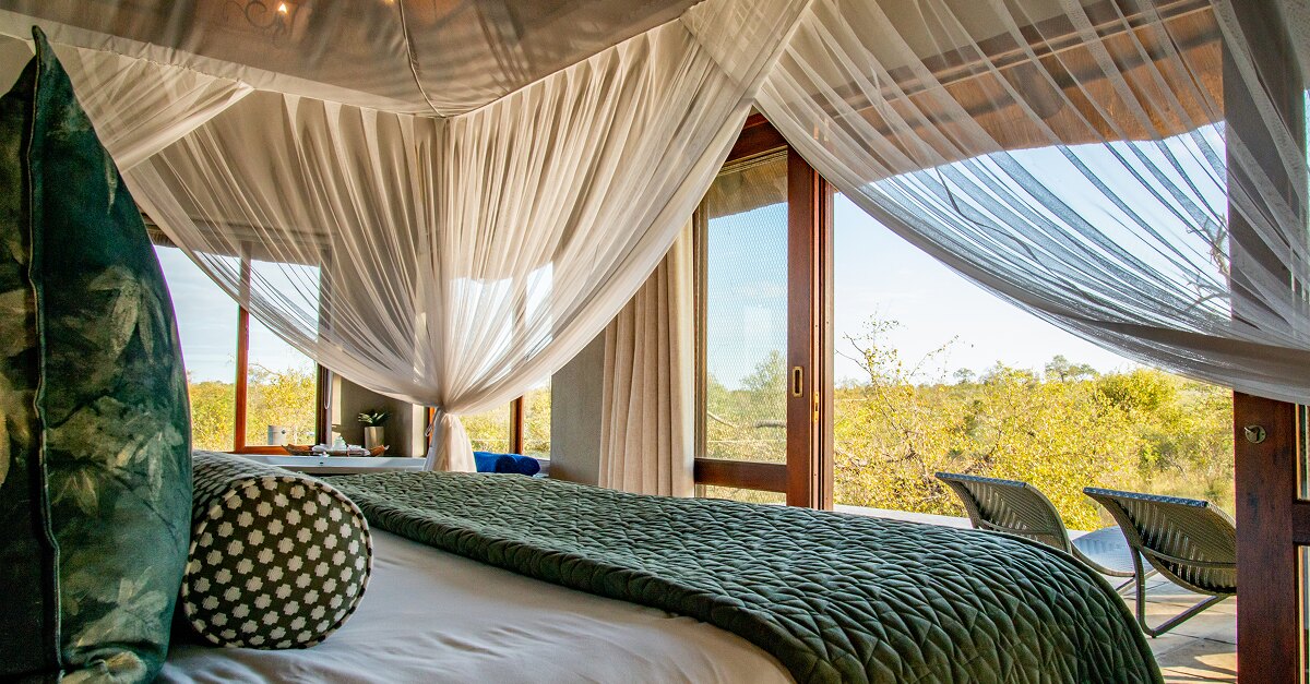 An Arathusa Safari Lodge water-facing suite with a large bed and glass doors opening onto a private verandah over the waterhole