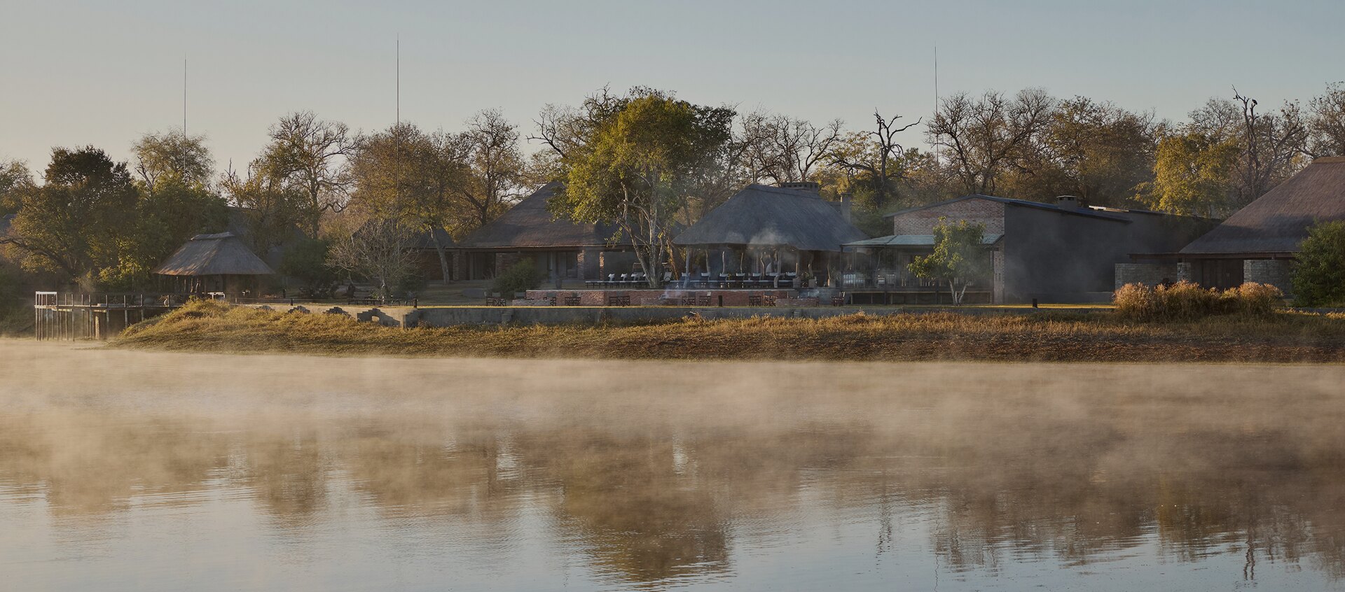 Arathusa Safari Lodge reflected in its misty waterhole at dawn