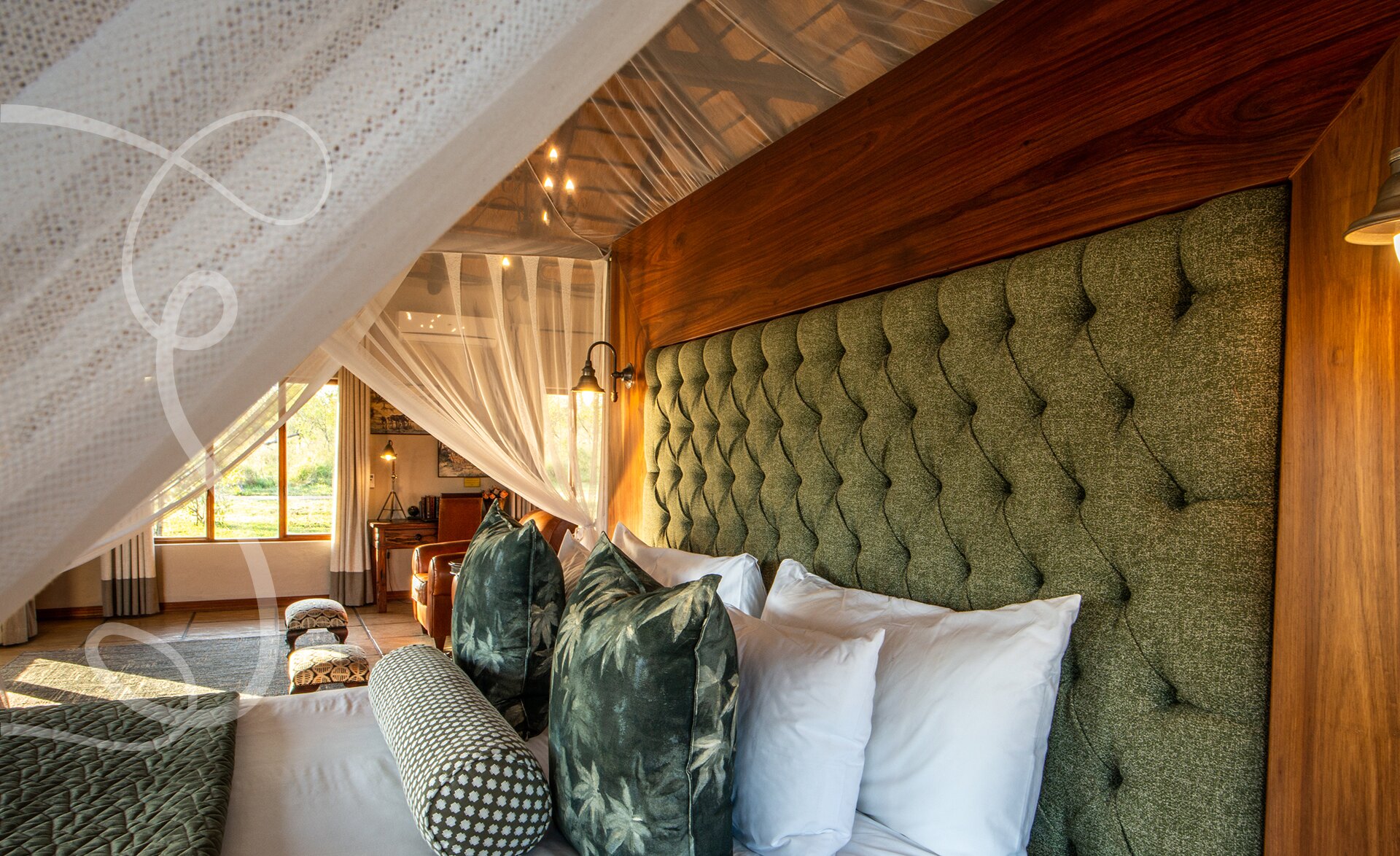 An Arathusa suite bed with a tufted green headboard and a draped mosquito net