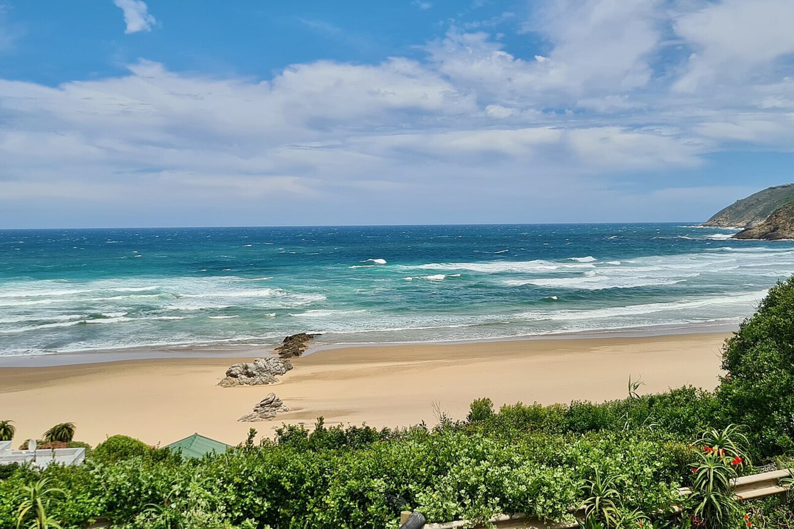 A golden Garden Route beach with gentle turquoise surf and forested hills behind