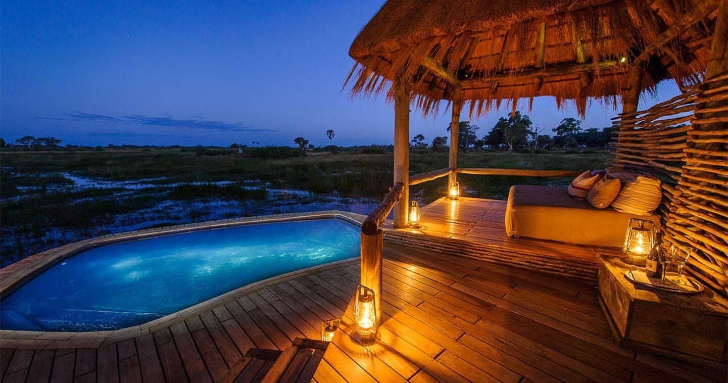 A private thatched deck and plunge pool at Mombo Camp lit at dusk over the Okavango floodplain
