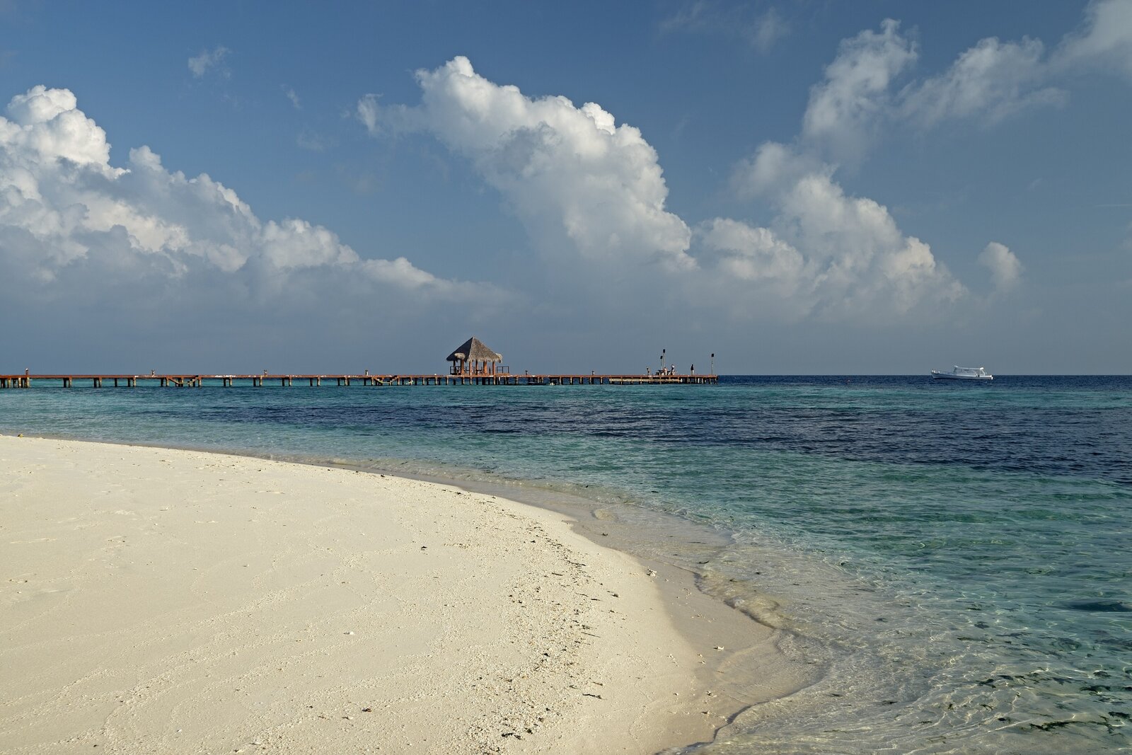 A white-sand Maldivian beach with a jetty under bright dry-season skies