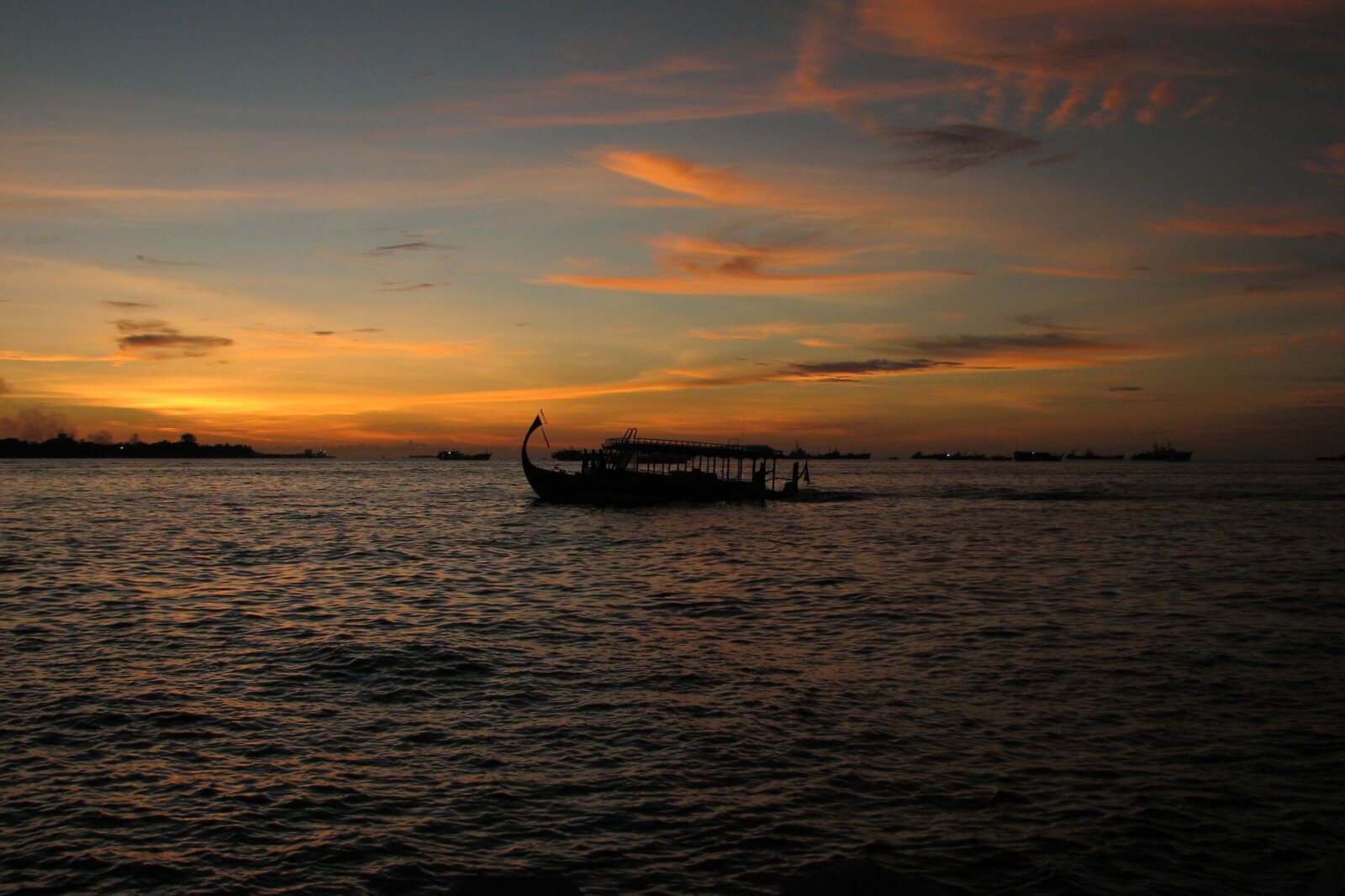 A traditional Maldivian dhoni boat silhouetted at sunset