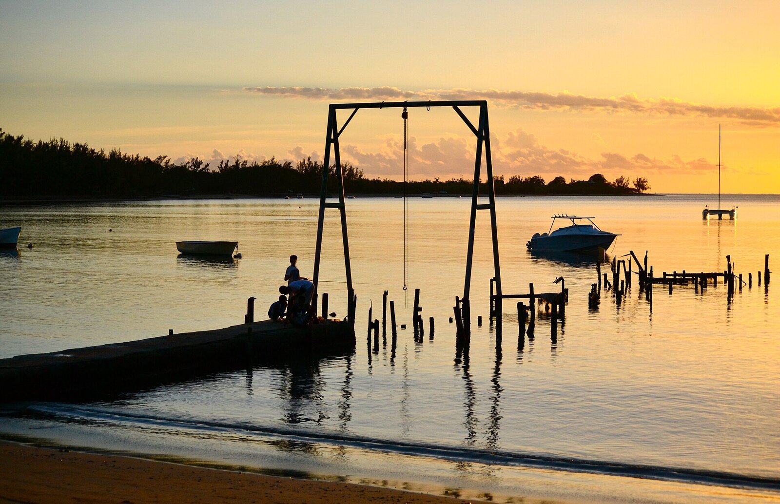 A wooden jetty reaching into a calm lagoon at sunset in Mauritius