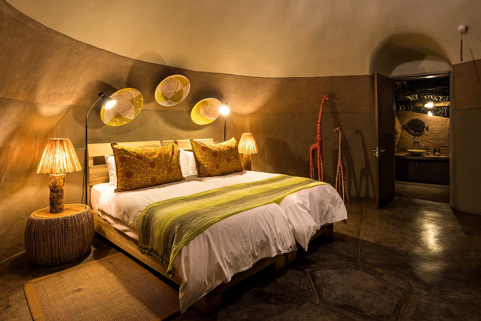 Bungalow interior with bed and rock-set walls at Camp Kipwe, Damaraland