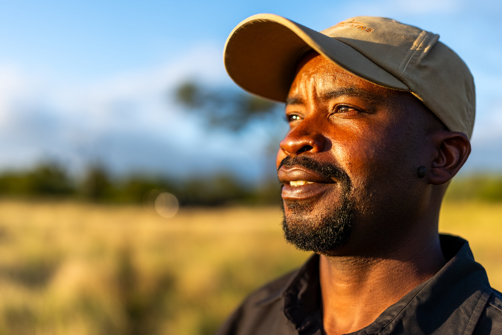 A Cheetah Plains field guide in a cap smiling in golden afternoon light in the bush