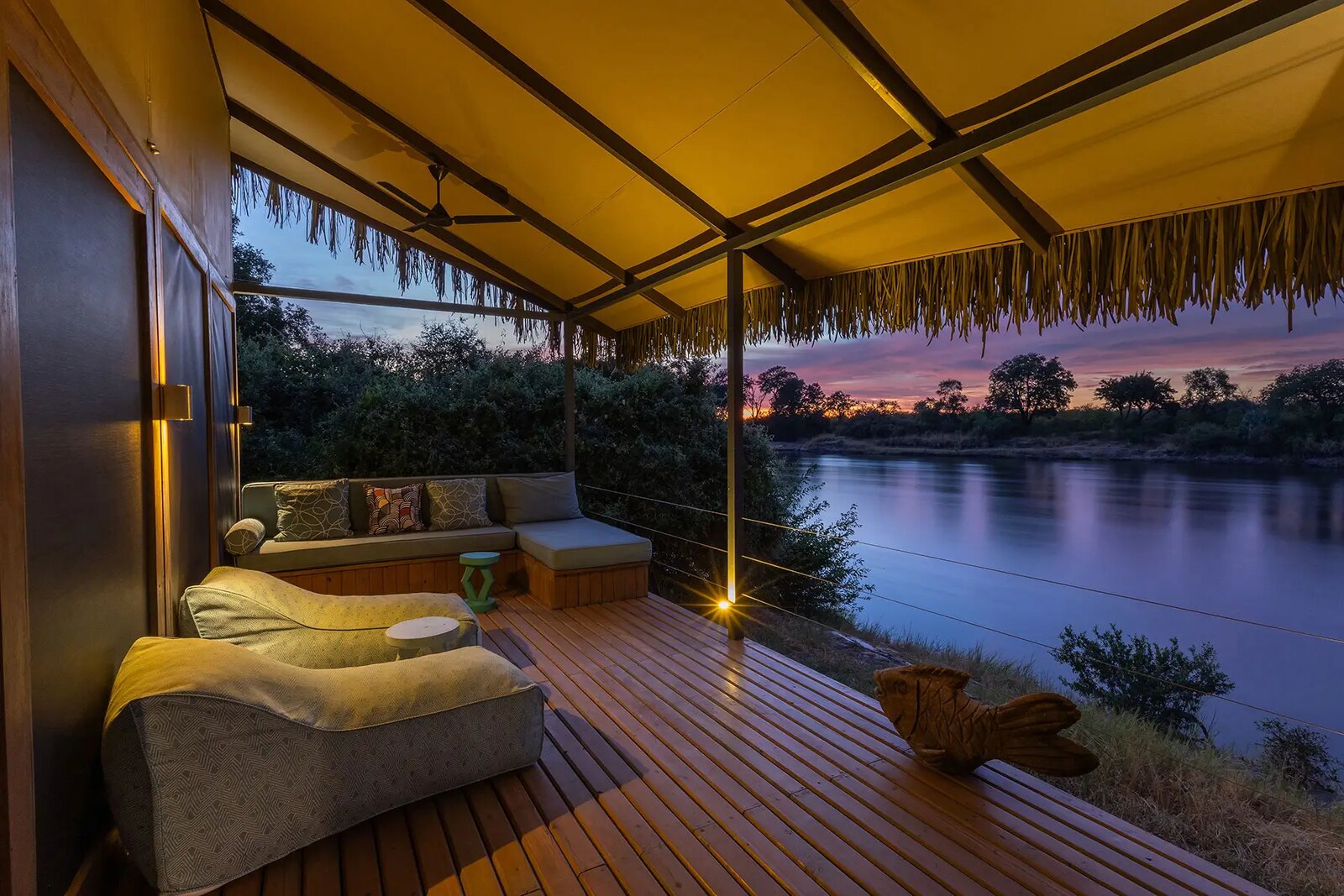 The private deck of a Chundu Island suite with a day bed above the Zambezi at dusk