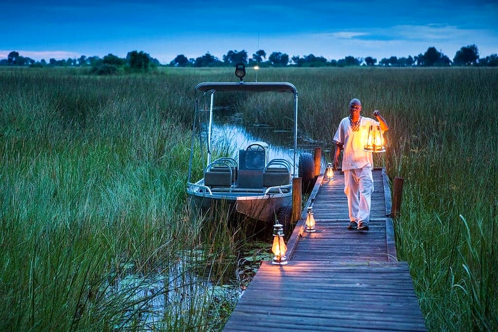 A guide walking a lantern-lit boardwalk to the water at Duba Plains, Okavango Delta