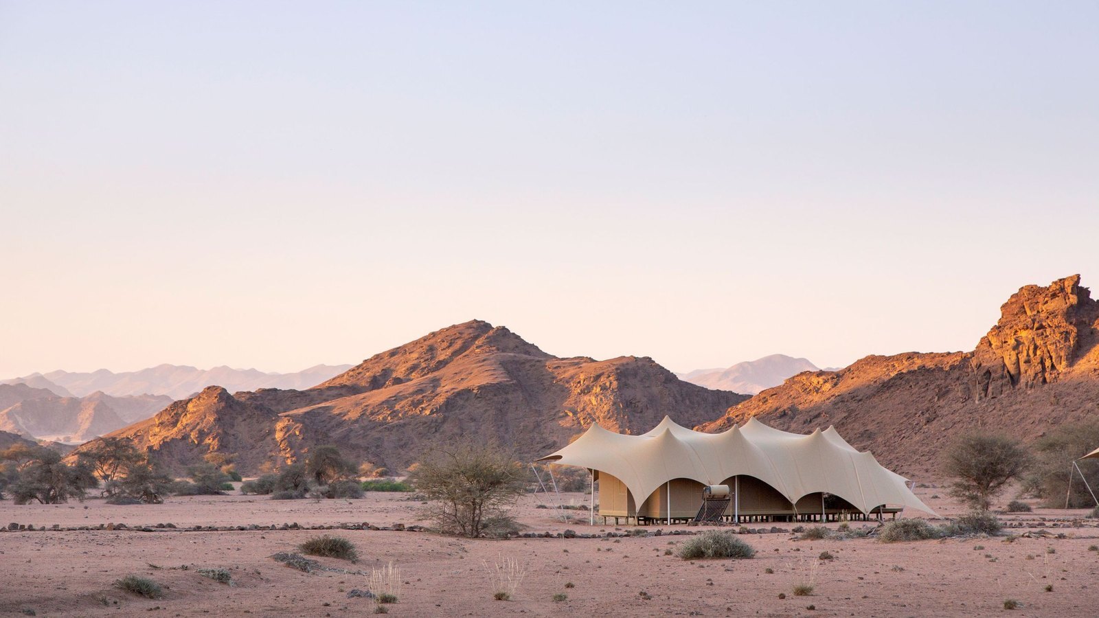 Hoanib Valley Camp tented suite with desert mountains and dry riverbed behind