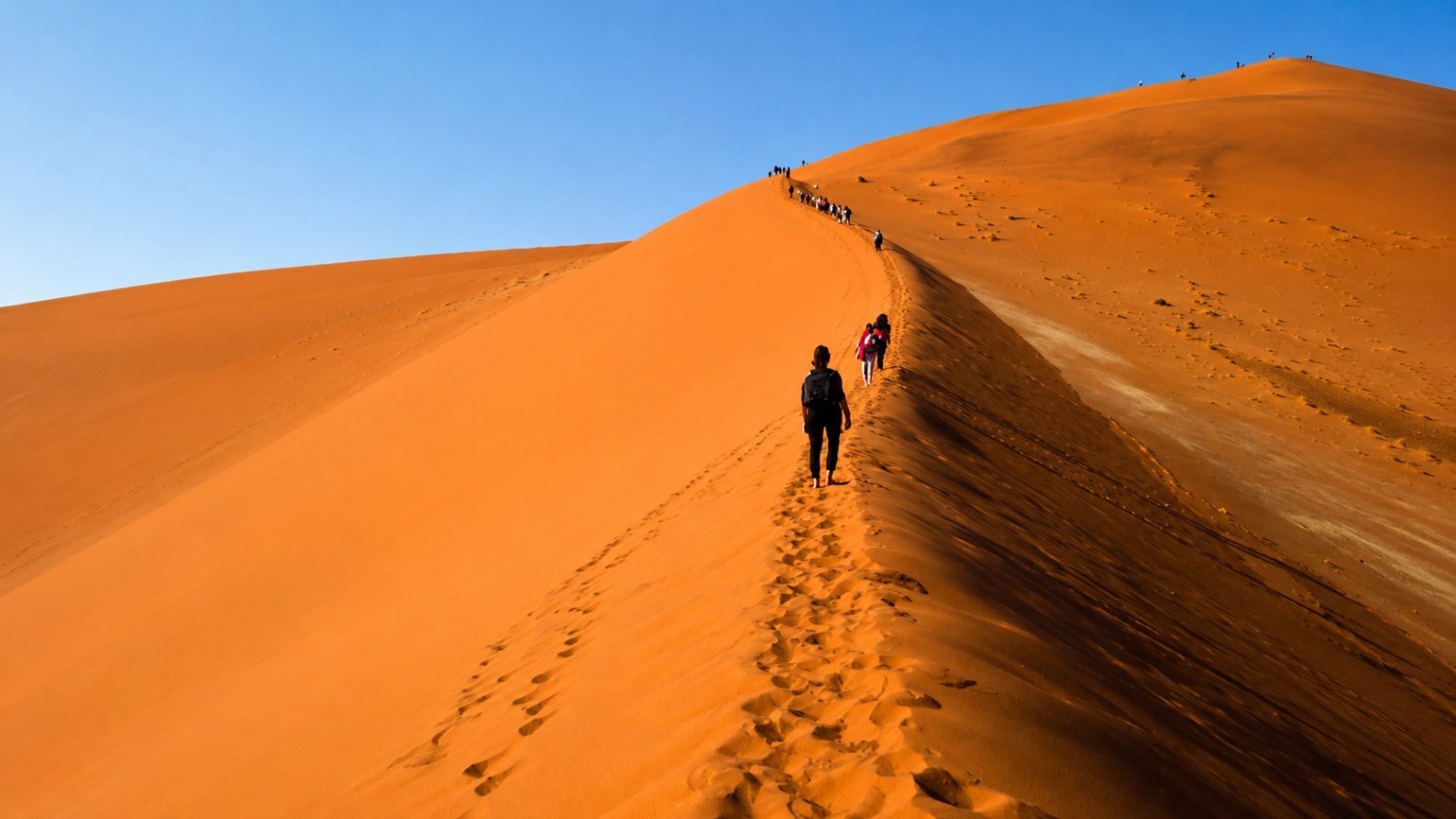 Family walking along a NamibRand nature trail at sunset with red dunes behind