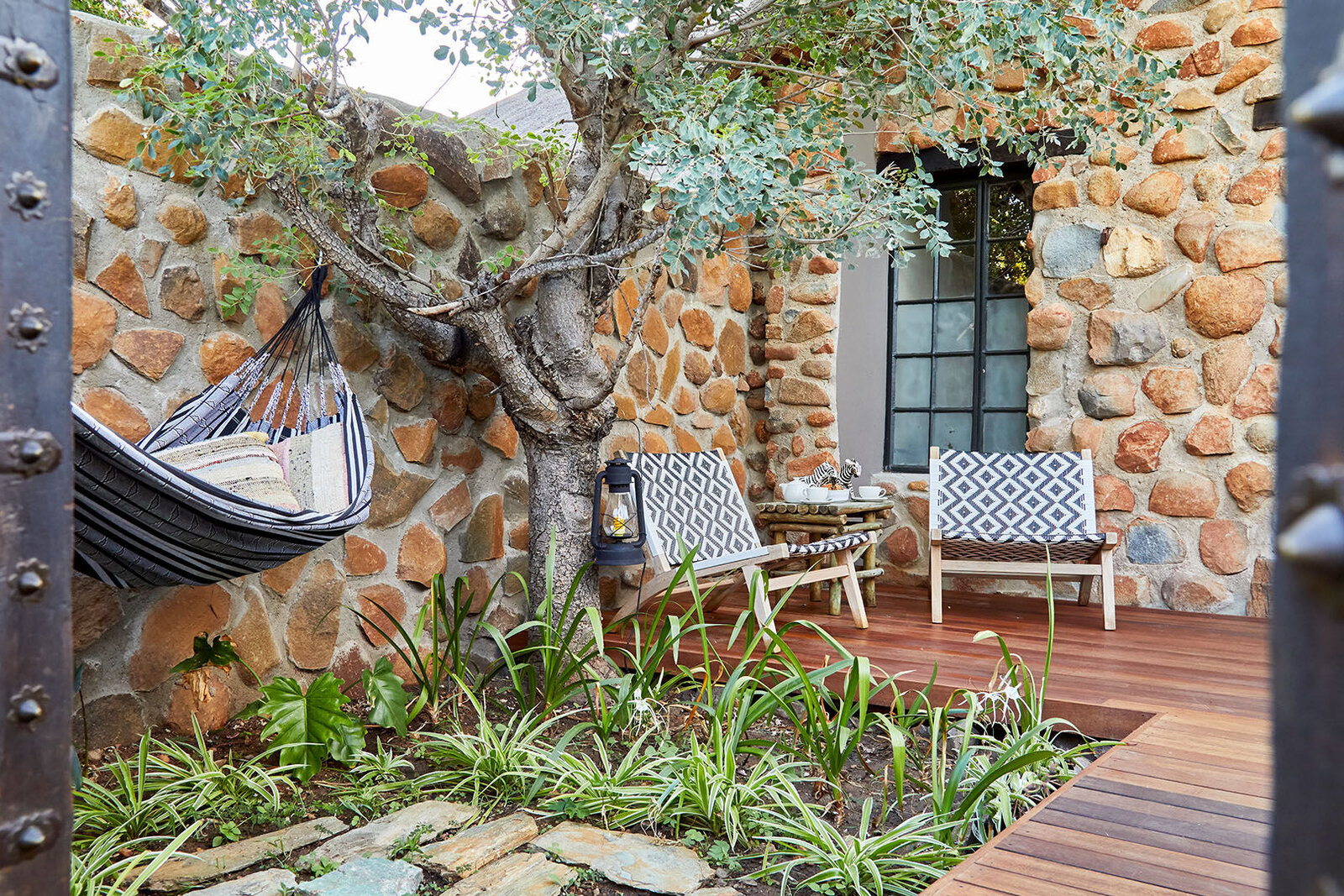 Four-poster bed with white drapes against a stone wall in a Geiger's Camp suite, Timbavati