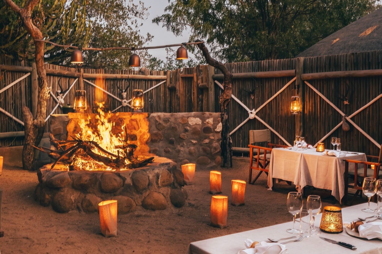 Boma at Geiger's Camp at dusk with a stone fire pit and strung lanterns, Timbavati