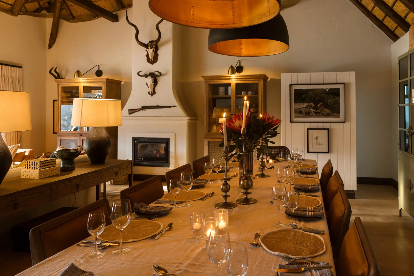 Jock Safari Lodge lounge interior with a stone fireplace, African art, skulls and warm amber lighting