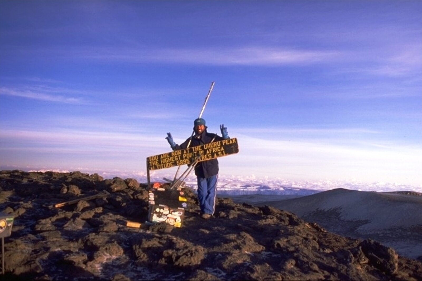 A climber holding the Uhuru Peak summit sign at dawn on Kilimanjaro